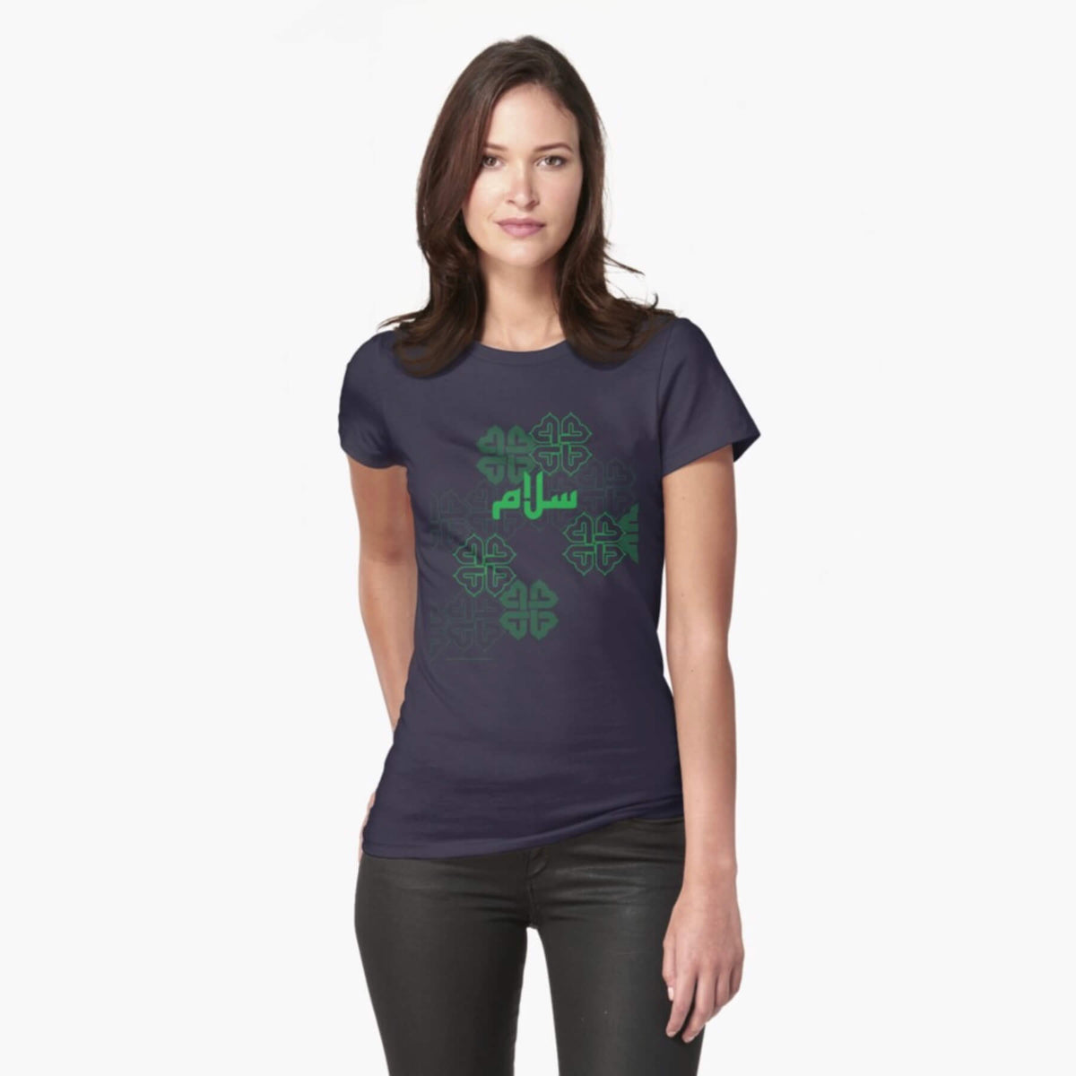 A white female model with hazel eyes and mid-brown shoulder length hair wears the Haluna Happy Names exclusive &#39;Salaam—Arabic Key Words&#39; design navy loosely fitted t-shirt and a pair of tight black jeans. The word &#39;salaam&#39; is written on the tshirt in green in Arabic using a kufic-style font, across the chest of the model against a complementary green patterned background print. The tshirt ends at the woman&#39;s hips and the image cuts off mid-thigh. 