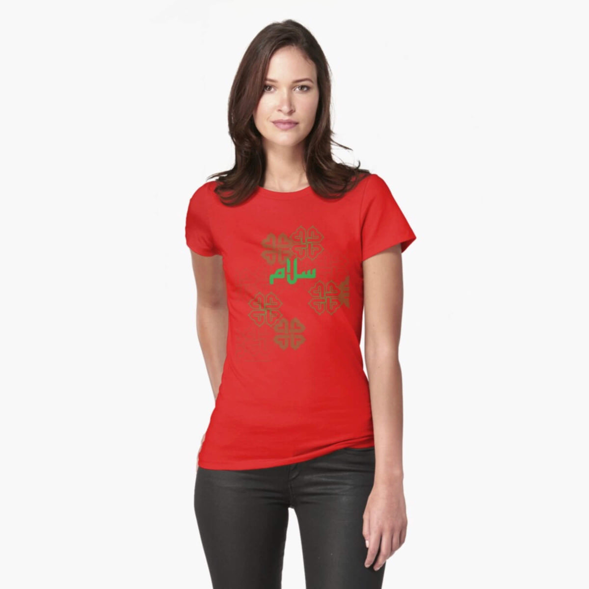 A white female model with hazel eyes and mid-brown shoulder length hair wears the Haluna Happy Names exclusive &#39;Salaam—Arabic Key Words&#39; design bright red loosely fitted t-shirt and a pair of tight black jeans. The word &#39;salaam&#39; is written on the tshirt in green in Arabic using a kufic-style font, across the chest of the model against a complementary green patterned background print. The tshirt ends at the woman&#39;s hips and the image cuts off mid-thigh.