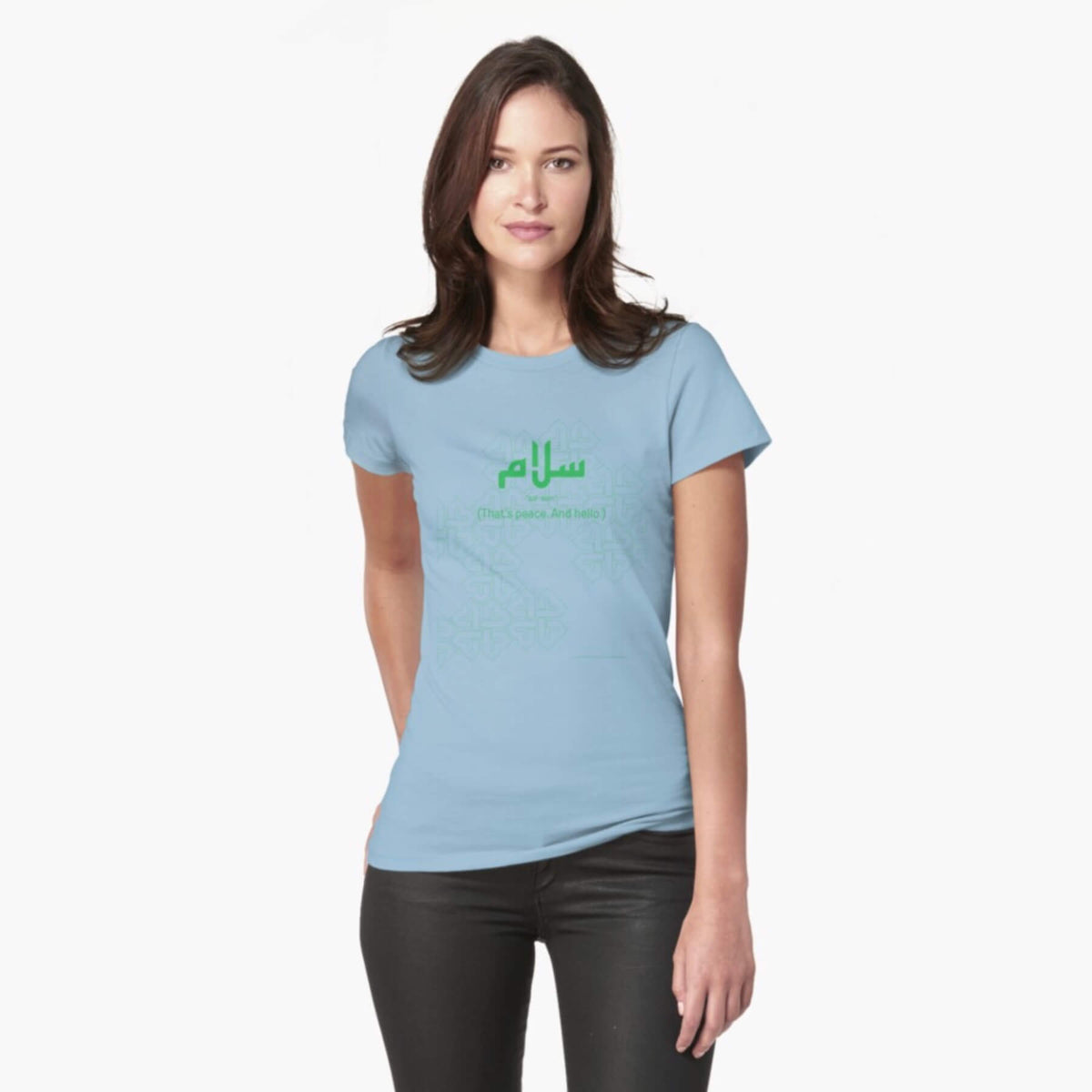 A white female model with hazel eyes and brown shoulder-length hair wears the Haluna Happy Names exclusive &#39;Salaam—Arabic Key Words&#39; design fitted t-shirt in sky blue marle ,and tight black jeans. The word &#39;salaam&#39; is written in green in Arabic with a kufic-style font, and beneath it in English the words &quot;Sal-aam&quot; and beneath that the words &#39;(That means peace. And hello)&#39;. The text is positioned on the tshirt so it falls across the chest of the model against a complementary green background pattern.
