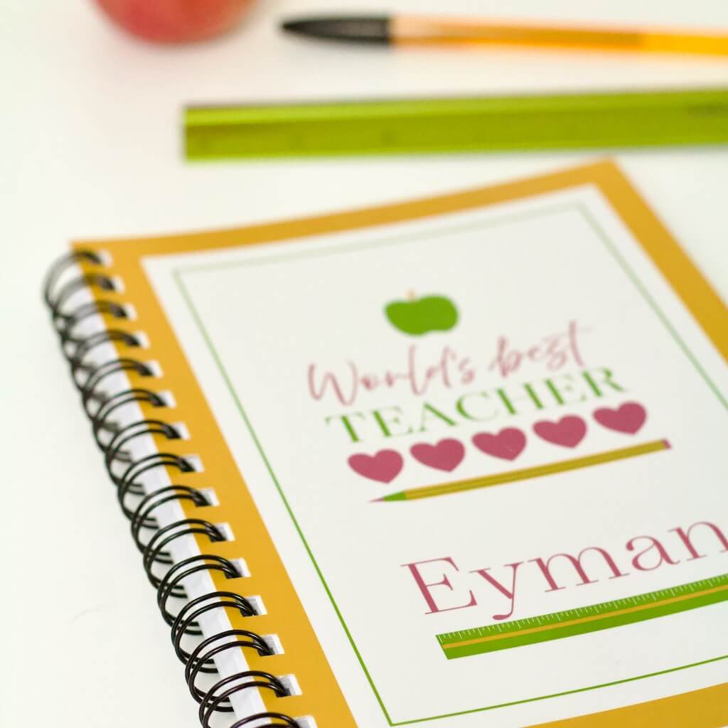 &#39;World&#39;s Best Teacher&#39; design in mustard shows teacher&#39;s name and ruler in sharp focus and slogan, hearts, apple and pencil elements soft and fuzzy. Perfect teacher gift.